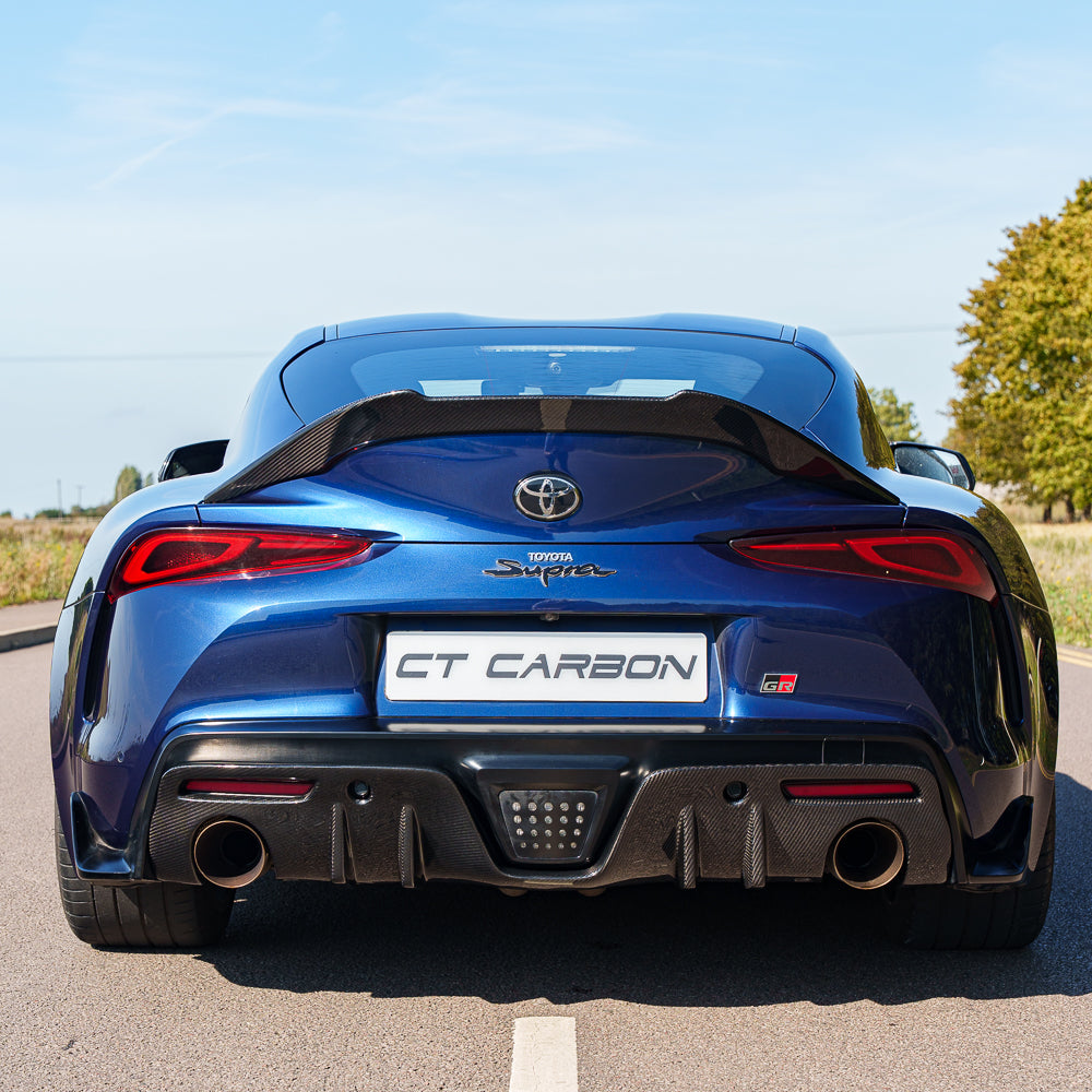 Carbon fiber diffuser add-on for Toyota Supra 2019+ A90 by CT Carbon, showing the sleek, textured finish on the vehicle's rear.