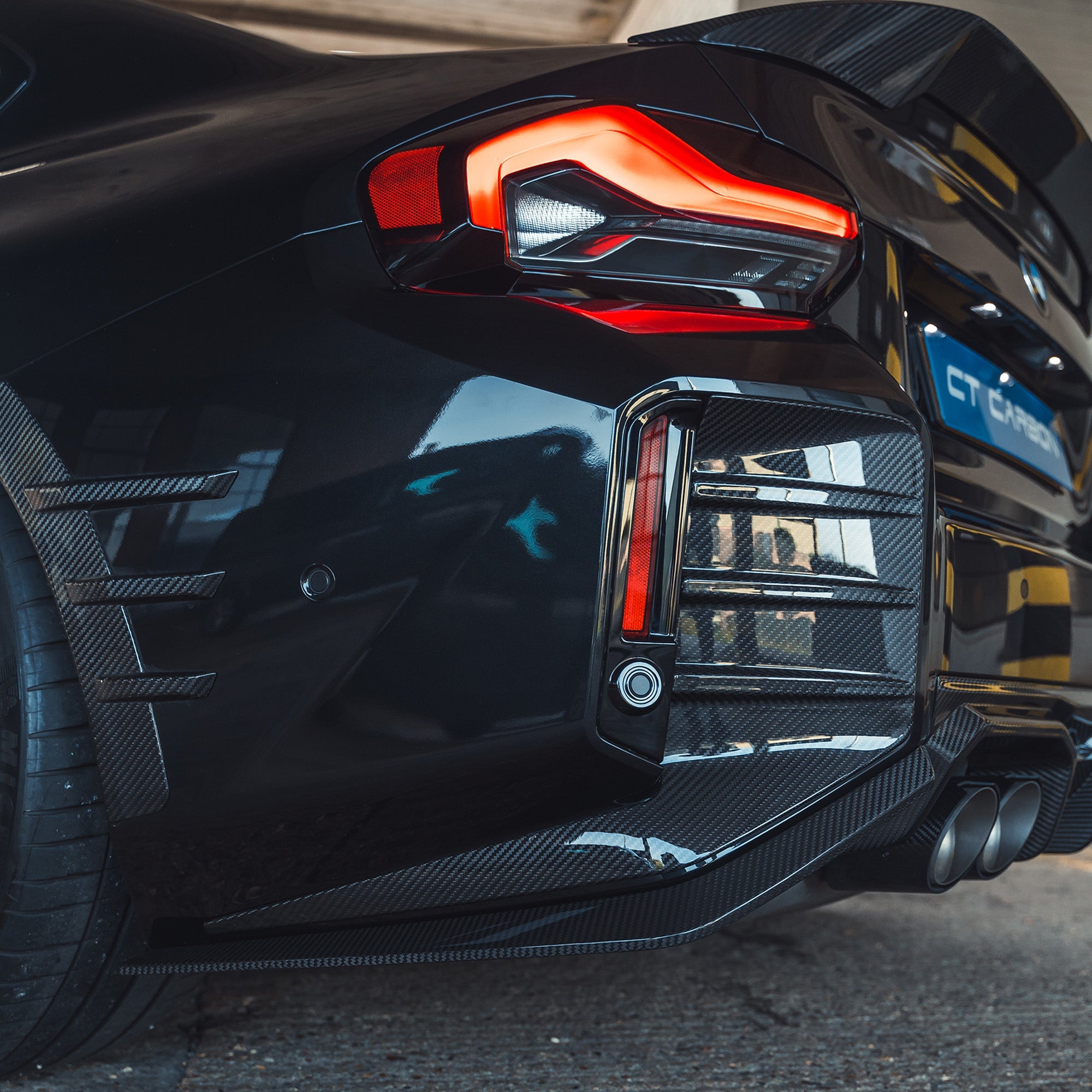 BMW G87 M2 carbon fiber rear bumper trim by CT Carbon, close-up showing sleek, lightweight automotive accessory with textured finish.