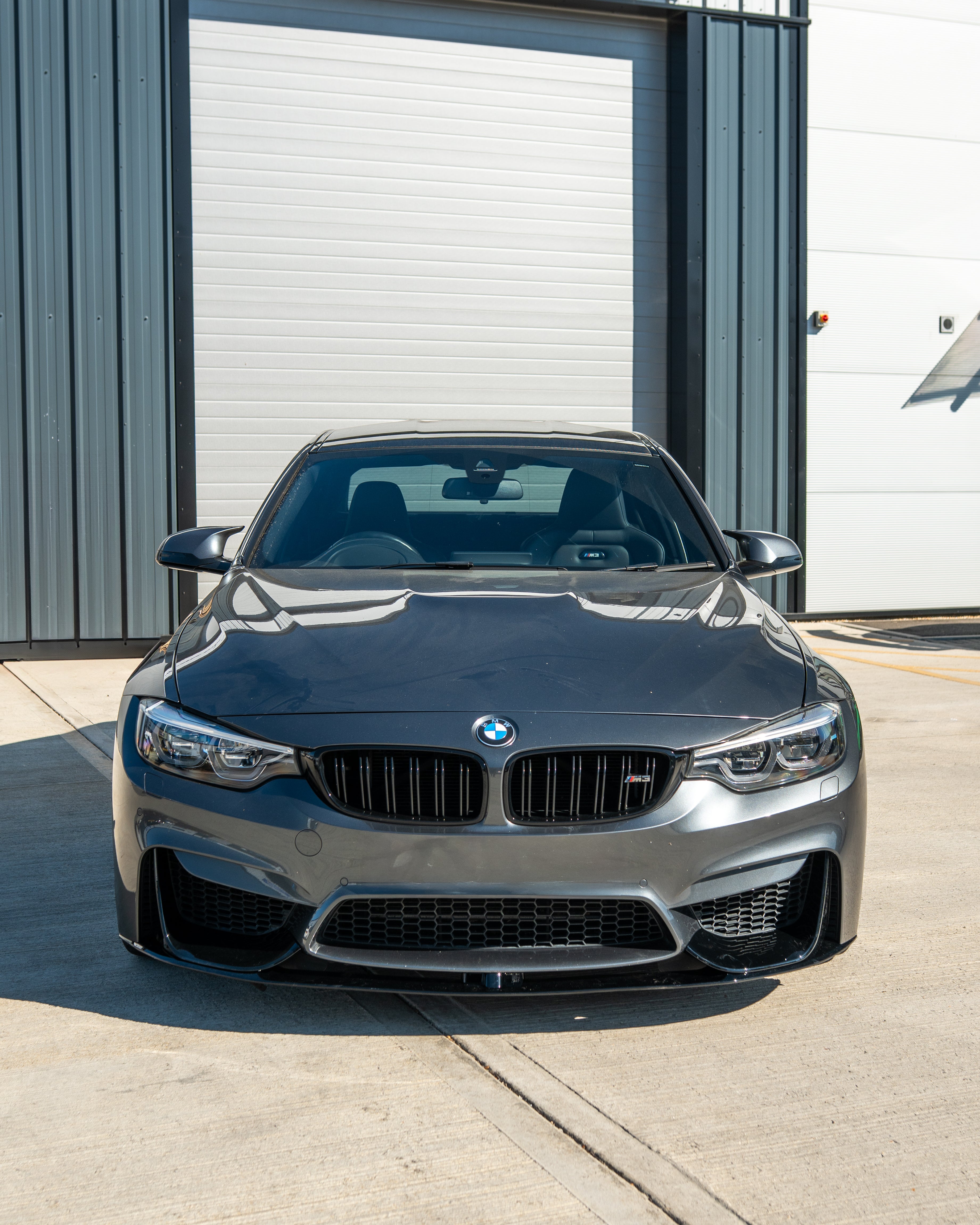 BMW M3 M4 F80 F82 F83 GLOSS BLACK splitter by CT Carbon visible on front of coupe, showcasing sleek aerodynamic design.