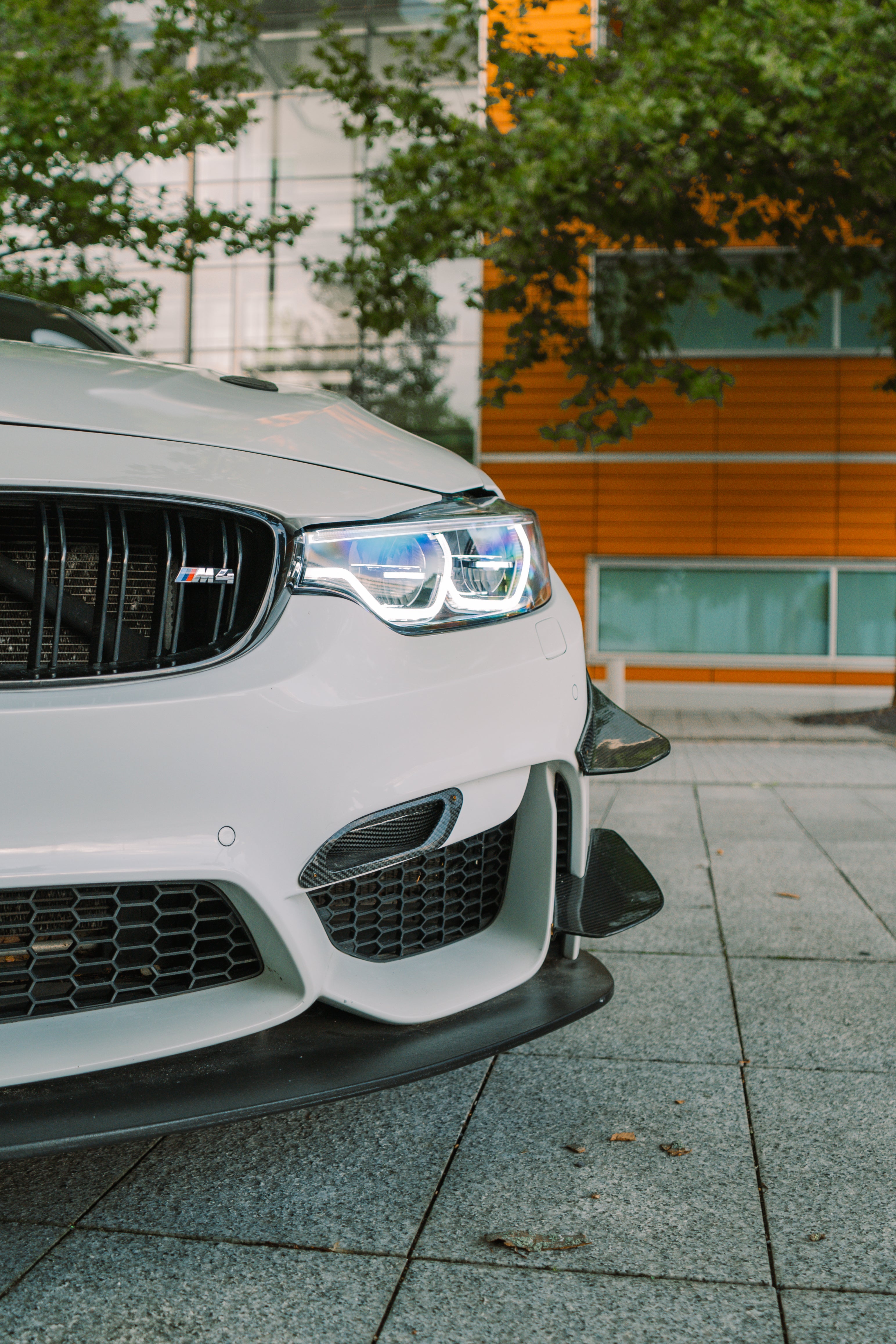 Close-up of a white BMW car's front grille and headlight on a city street.