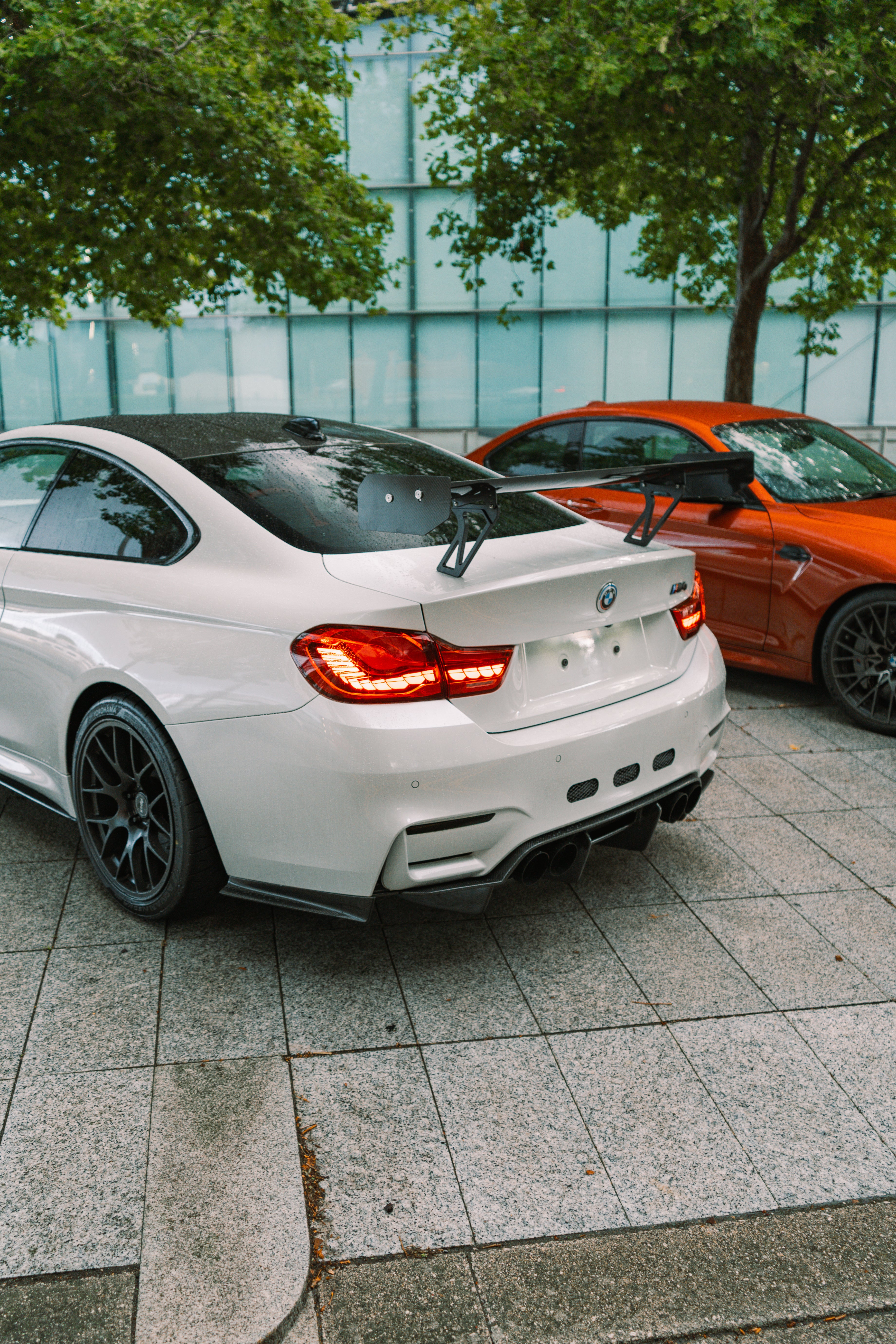 White sports car with black spoiler parked on a sidewalk next to an orange car.