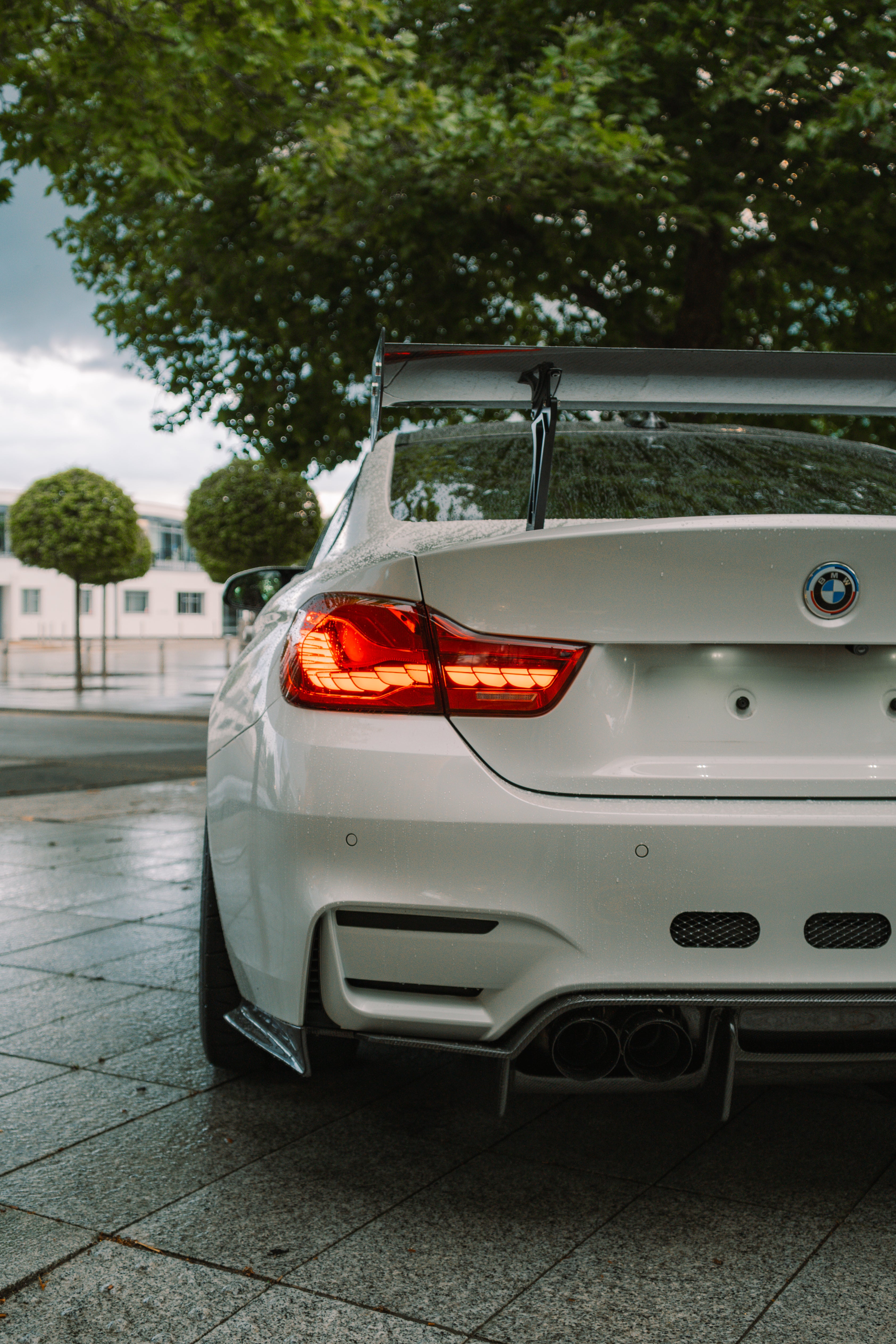 White BMW car with a spoiler on a paved surface with trees in the background