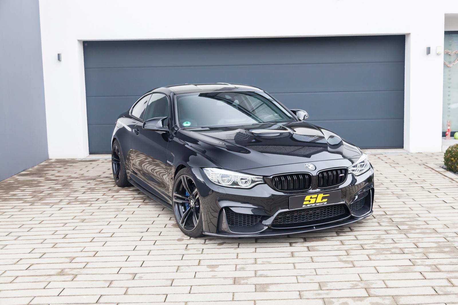 ST Suspension coilovers for BMW F80 M3, F82 M4, F83 M4 with adjustable damping and top mounts, shown on a black coupe.
