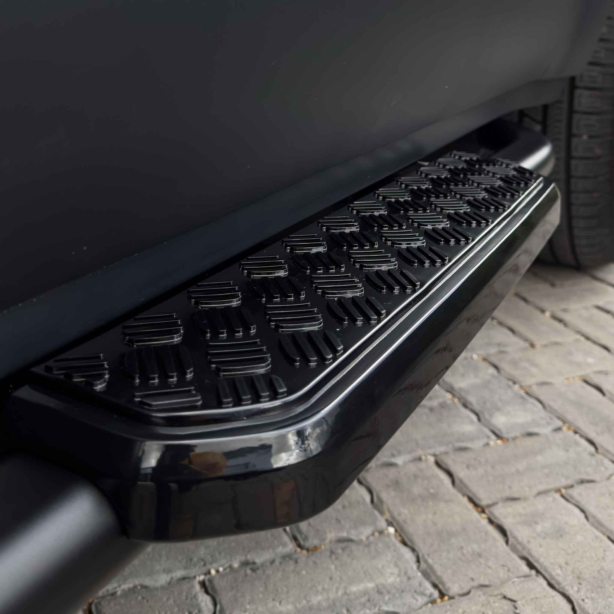 Land Rover Defender L663 90 side steps by CT Carbon, black aluminum accessories mounted along the vehicle's side for easier access.